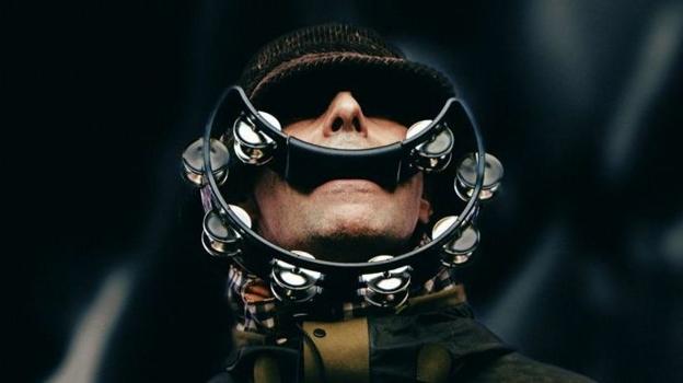 Liam Gallagher of Oasis with his eyes shaded by the peak of his hat, with a smile-shaped tambourine in his mouth