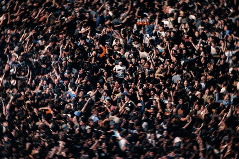 A man in a classic light blue Oasis t-shirt (centre) surveys the scene as all hell breaks loose around him during one of the band's reunion concerts