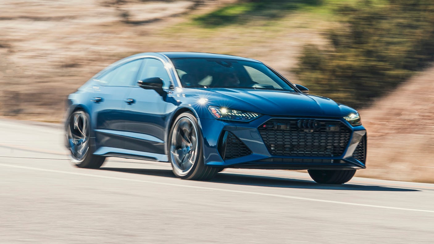 front three quarter view of blue sedan driving on road with blurred hillside background.