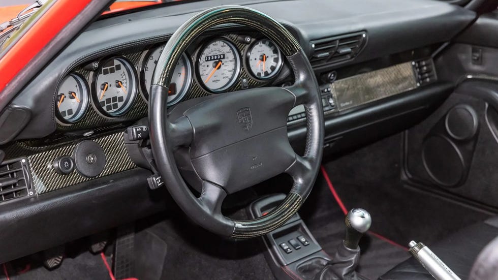Interior view of a sports car dashboard with gauges, steering wheel, and gear shift visible.