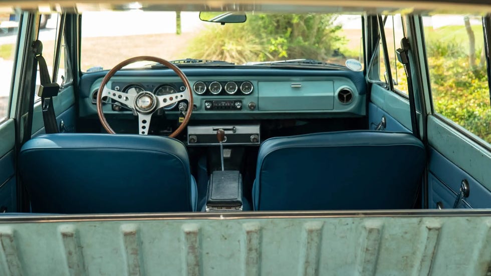 Interior view of a vintage vehicle with blue seats and a wooden steering wheel.