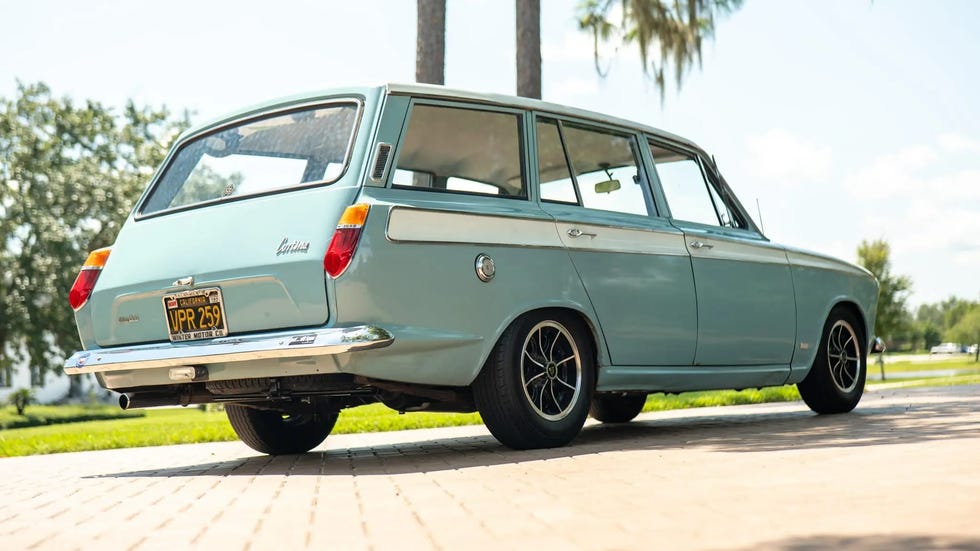 Classic light blue station wagon parked on a brick pathway with green grass and palm trees in the background.