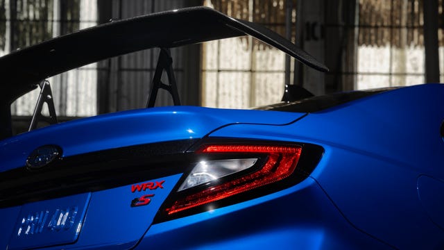 Blue Subaru WRX with an aerodynamic spoiler and illuminated taillights, highlighting its sporty design.